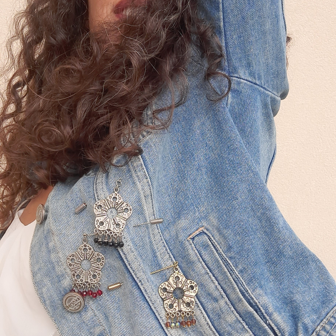 Close-up of a denim jacket with decorative pins hanging from it.